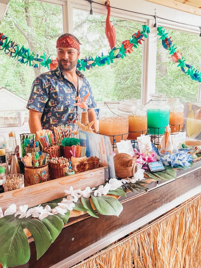 A Freaki Tiki bartender behind a tropical bar lined with colorful cocktails